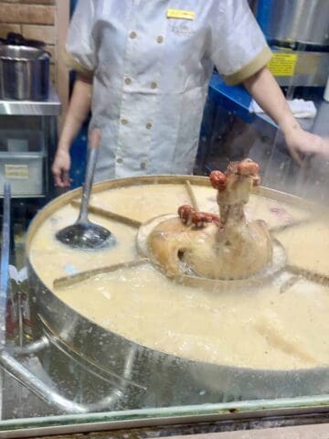 Chicken head sticking out of a giant vat of soup.